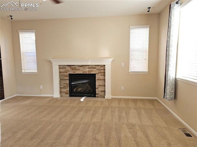 unfurnished living room featuring a stone fireplace, carpet floors, ceiling fan, and a wealth of natural light