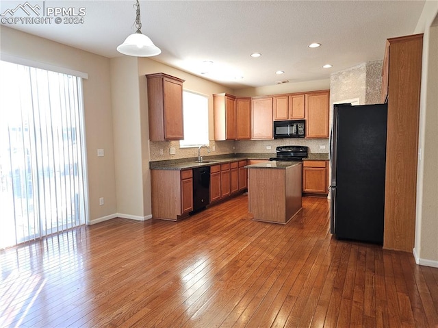 kitchen featuring dark wood-type flooring, hanging light fixtures, sink, black appliances, and a center island