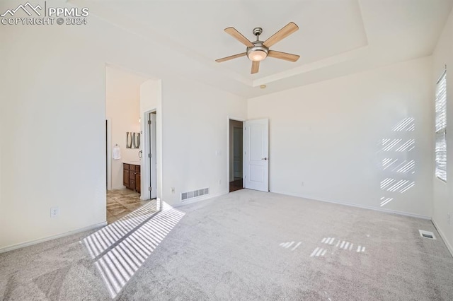 unfurnished bedroom featuring light carpet, a tray ceiling, ensuite bath, and ceiling fan