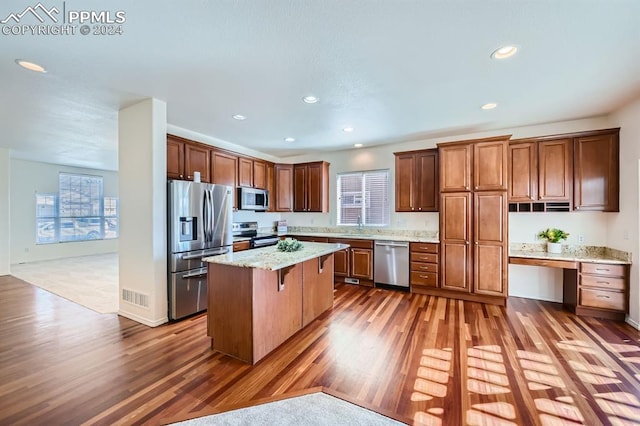 kitchen with a center island, dark wood-type flooring, light stone countertops, appliances with stainless steel finishes, and a breakfast bar area