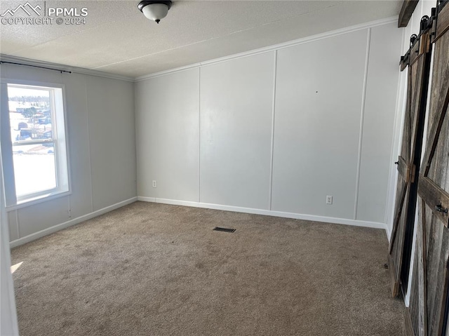 spare room featuring a textured ceiling, a barn door, carpet floors, and ornamental molding