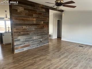 unfurnished living room featuring hardwood / wood-style flooring, ceiling fan, and wooden walls