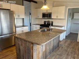 kitchen with hanging light fixtures, white cabinets, stainless steel appliances, and a center island with sink