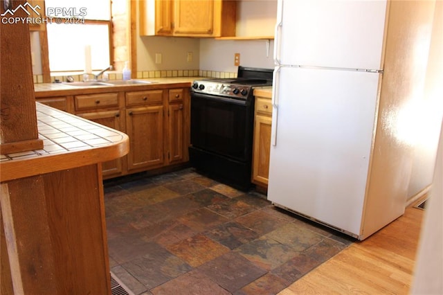 kitchen featuring tile counters, black range with electric cooktop, sink, white refrigerator, and dark hardwood / wood-style flooring