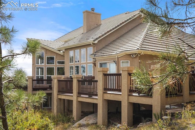 back of house with a wooden deck, stucco siding, a tile roof, and a chimney