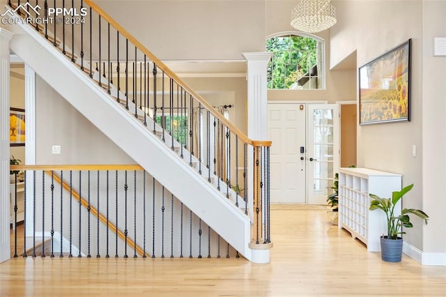 foyer entrance with ornate columns, a notable chandelier, a high ceiling, and hardwood / wood-style floors