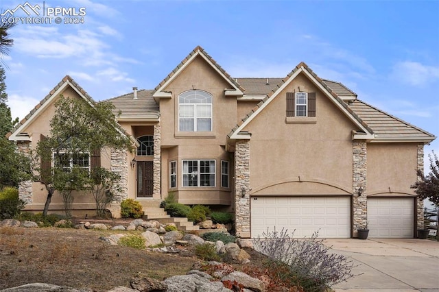 traditional home featuring driveway, stone siding, and stucco siding