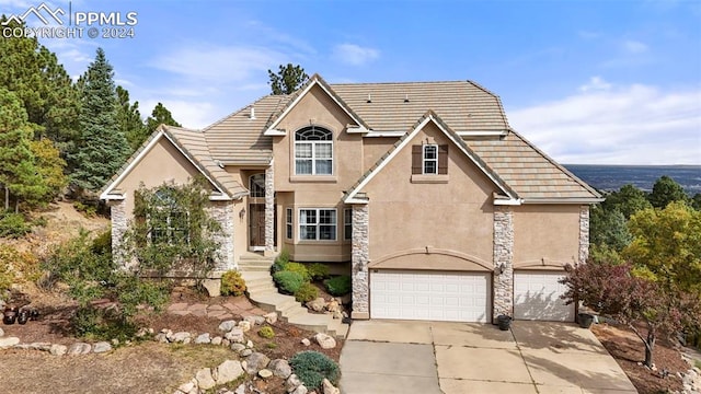 traditional-style house featuring stucco siding, driveway, a tile roof, and stone siding