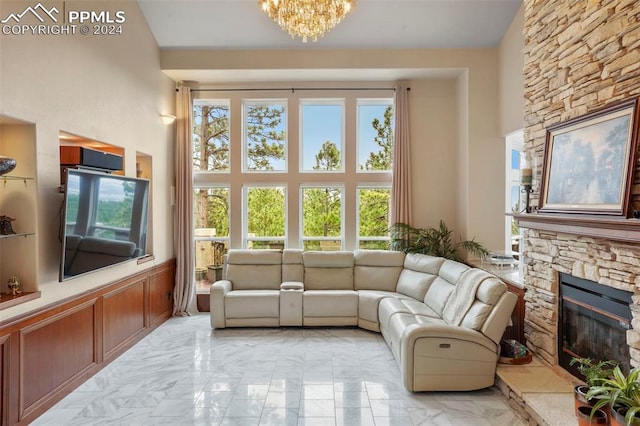 living area featuring a stone fireplace, a towering ceiling, a notable chandelier, a wainscoted wall, and marble finish floor