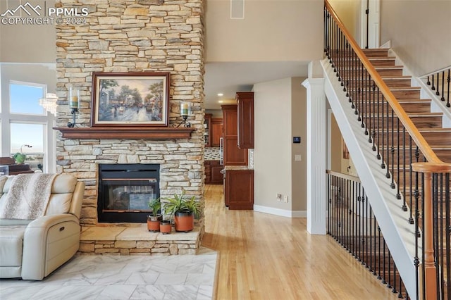 living area with a high ceiling, a stone fireplace, light wood-style flooring, baseboards, and stairway