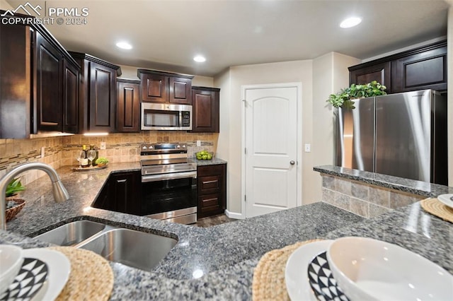 kitchen with dark brown cabinetry, sink, stainless steel appliances, tasteful backsplash, and dark stone counters