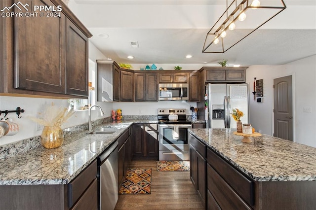 kitchen with appliances with stainless steel finishes, sink, a kitchen island, decorative light fixtures, and dark wood-type flooring