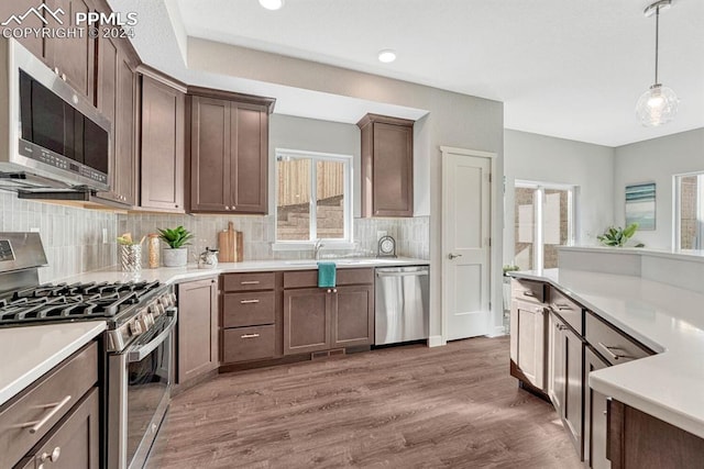 kitchen with appliances with stainless steel finishes, dark brown cabinetry, pendant lighting, dark wood-type flooring, and decorative backsplash