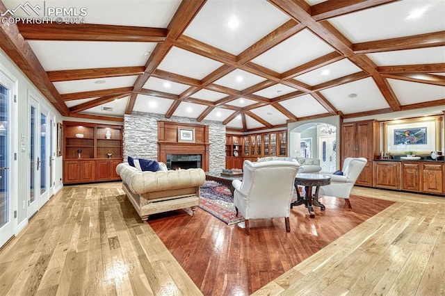 living room featuring vaulted ceiling with beams, coffered ceiling, a stone fireplace, and light hardwood / wood-style floors