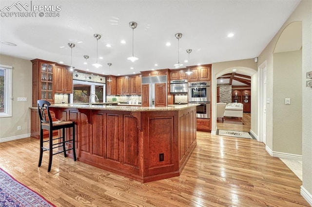 kitchen with light wood-type flooring, pendant lighting, double oven, light stone counters, and paneled refrigerator