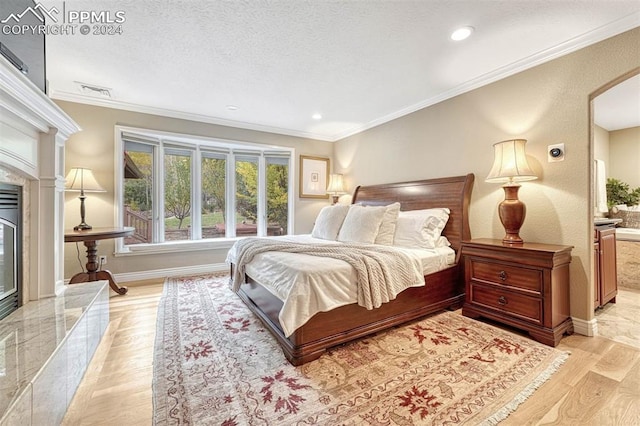 bedroom featuring a high end fireplace, a textured ceiling, ornamental molding, light hardwood / wood-style floors, and ensuite bath