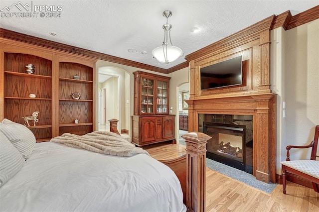 bedroom featuring a large fireplace, a textured ceiling, ornamental molding, and light hardwood / wood-style flooring