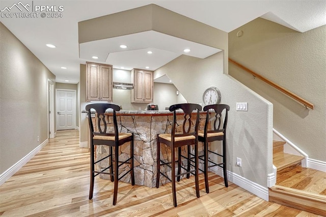 kitchen with light brown cabinets, a kitchen breakfast bar, kitchen peninsula, ventilation hood, and light wood-type flooring