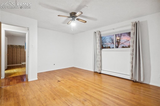 empty room with baseboard heating, light wood-type flooring, and ceiling fan