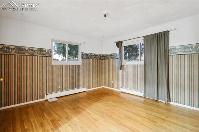 unfurnished room with baseboard heating, hardwood / wood-style flooring, and plenty of natural light