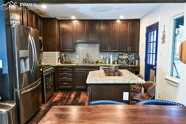 kitchen featuring light stone counters, tasteful backsplash, appliances with stainless steel finishes, dark hardwood / wood-style floors, and a center island