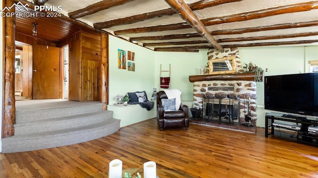 living room featuring hardwood / wood-style flooring, beamed ceiling, and a stone fireplace