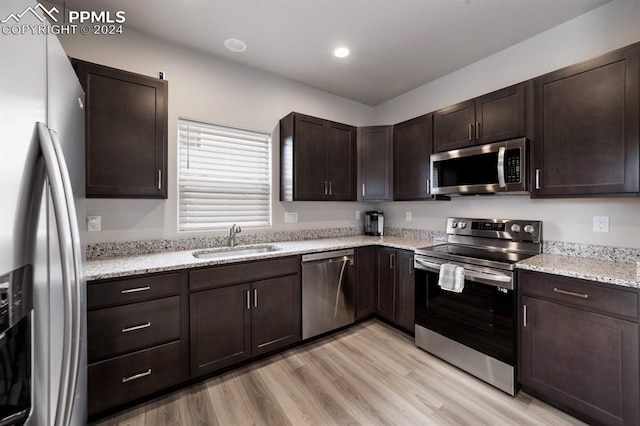 kitchen featuring light stone countertops, sink, appliances with stainless steel finishes, dark brown cabinetry, and light hardwood / wood-style flooring