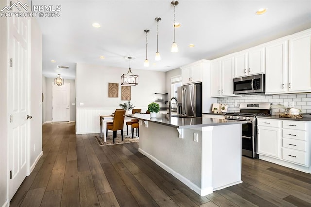 kitchen featuring stainless steel appliances, white cabinetry, hanging light fixtures, an island with sink, and dark hardwood / wood-style flooring