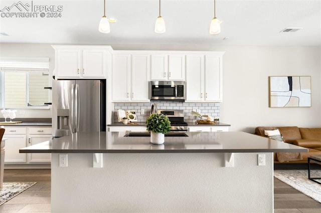 kitchen with white cabinets, appliances with stainless steel finishes, hanging light fixtures, and a center island with sink