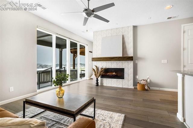 living room with a tiled fireplace, dark wood-type flooring, and ceiling fan