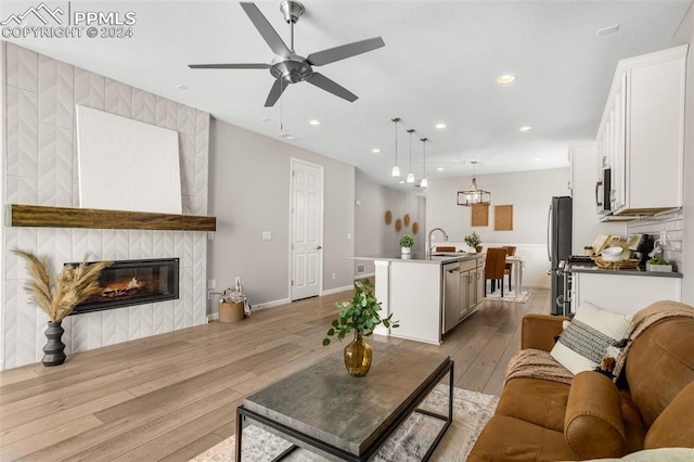 living room featuring light wood-type flooring, a fireplace, ceiling fan, and sink