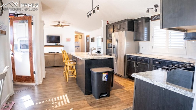 kitchen featuring light wood-type flooring, vaulted ceiling, a breakfast bar area, and an island with sink