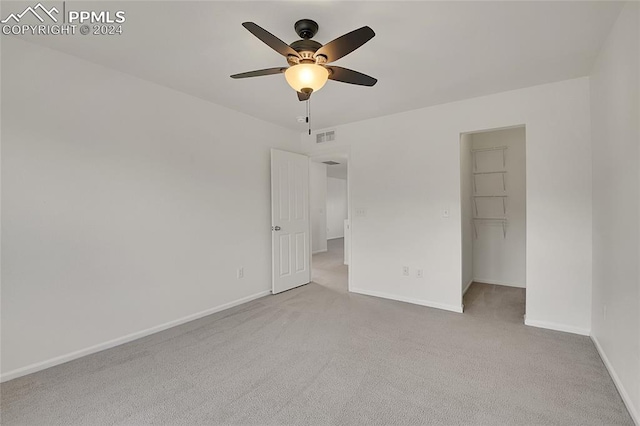 unfurnished bedroom featuring a spacious closet, light colored carpet, a closet, and ceiling fan