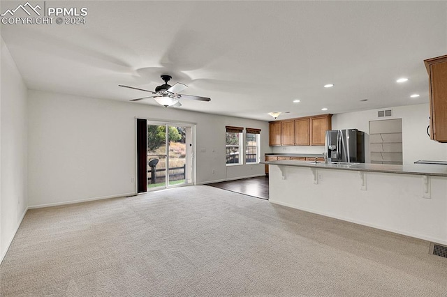 kitchen featuring kitchen peninsula, stainless steel fridge, carpet, ceiling fan, and a kitchen breakfast bar