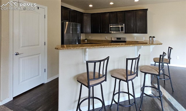 kitchen with light stone counters, dark hardwood / wood-style floors, stainless steel appliances, and a breakfast bar