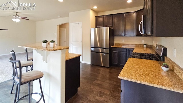 kitchen featuring a kitchen island, a kitchen bar, light stone counters, stainless steel appliances, and dark wood-type flooring