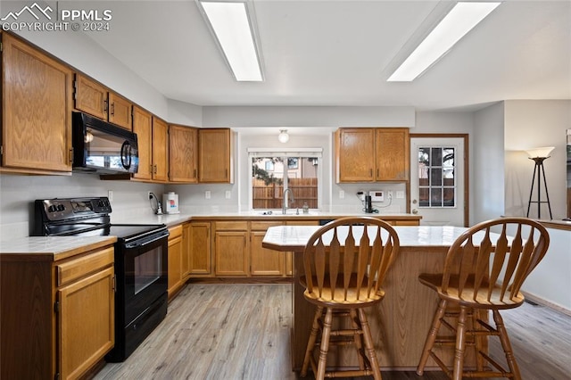 kitchen with a kitchen bar, light hardwood / wood-style floors, a center island, black appliances, and sink