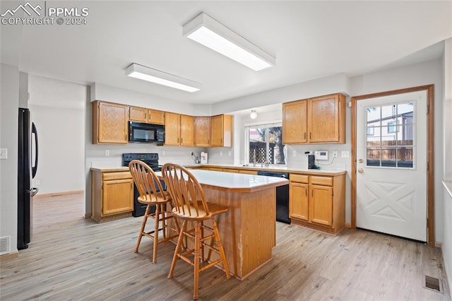 kitchen featuring light hardwood / wood-style floors, sink, a breakfast bar, black appliances, and a kitchen island