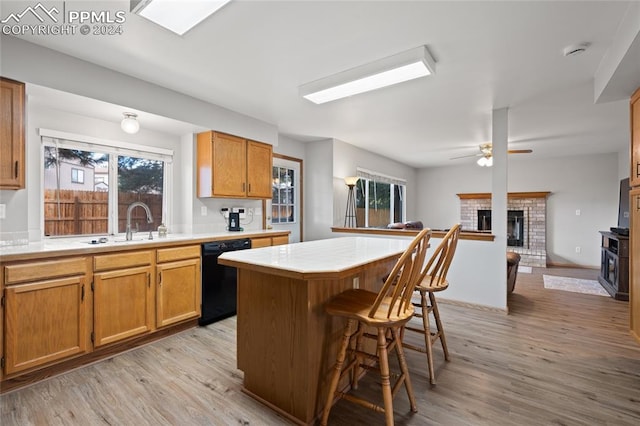 kitchen with a fireplace, a kitchen island, dishwasher, and light hardwood / wood-style flooring