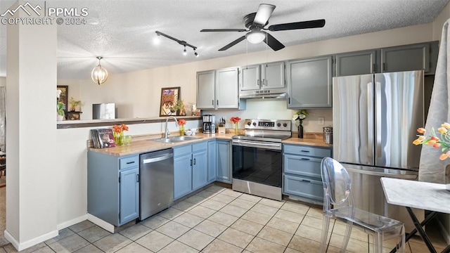 kitchen with a textured ceiling, appliances with stainless steel finishes, hanging light fixtures, and sink