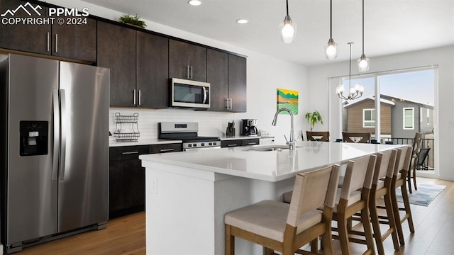 kitchen featuring sink, an island with sink, decorative light fixtures, appliances with stainless steel finishes, and hardwood / wood-style flooring