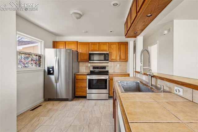 kitchen with tile counters, sink, appliances with stainless steel finishes, and tasteful backsplash