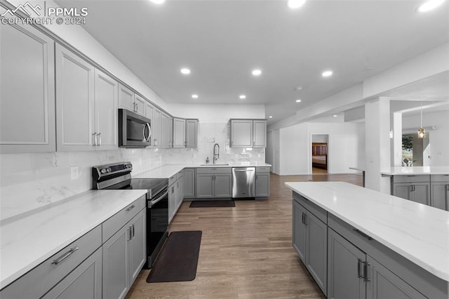 kitchen with gray cabinetry, sink, hardwood / wood-style floors, decorative backsplash, and appliances with stainless steel finishes