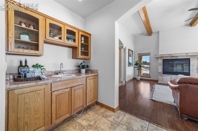 bar featuring light wood-type flooring, light stone counters, ceiling fan, sink, and beamed ceiling