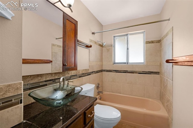 full bathroom featuring tiled shower / bath, vanity, toilet, and tile walls