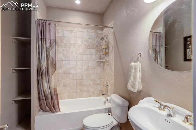 bathroom featuring a textured wall, toilet, shower / tub combo with curtain, and a sink