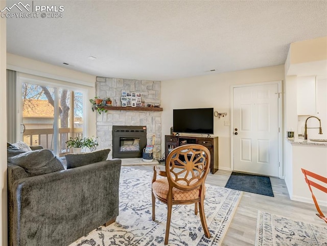 living room featuring a textured ceiling, sink, light wood-type flooring, and a fireplace