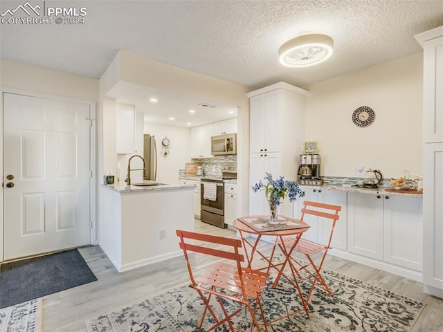 kitchen featuring appliances with stainless steel finishes, light wood-type flooring, light stone counters, a textured ceiling, and white cabinets