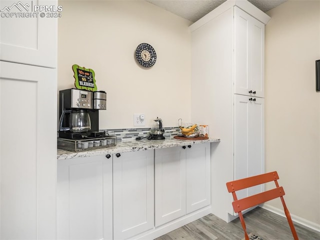 bar with white cabinets, a textured ceiling, light hardwood / wood-style flooring, and light stone counters