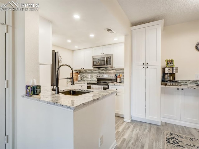 kitchen with light stone countertops, stainless steel appliances, sink, white cabinets, and light hardwood / wood-style floors